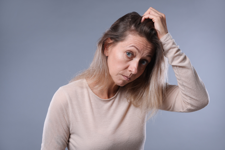 Woman with blonde hair touching her head against a gray background