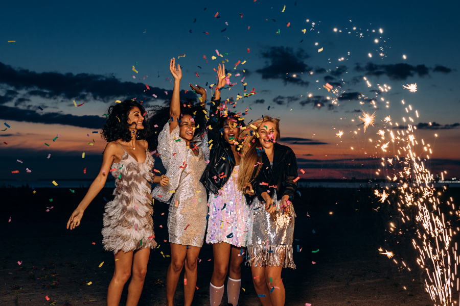 Group of friends celebrating the New Year outdoors at dusk with confetti and sparklers.