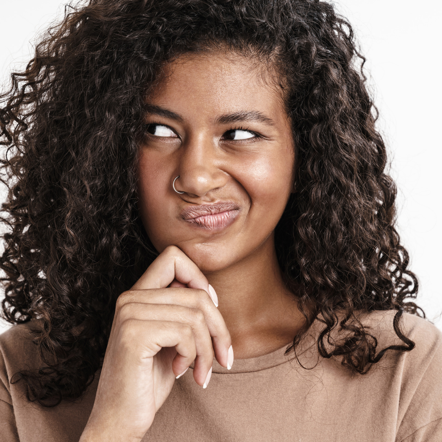 A close-up portrait of a smiling woman with curly dark hair, wearing a brown crew-neck top and a silver nose ring, looking to the side against a plain white background.